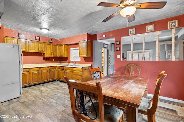 dining space featuring a textured ceiling, light wood-type flooring, ceiling fan, and sink