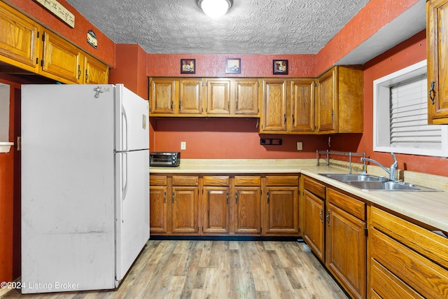 kitchen with white refrigerator, sink, a textured ceiling, and light hardwood / wood-style flooring