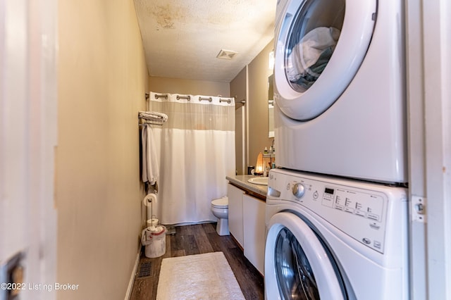 clothes washing area with a textured ceiling, dark hardwood / wood-style flooring, and stacked washing maching and dryer