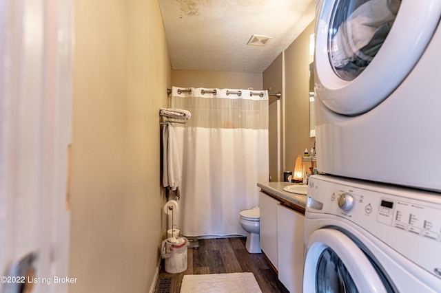 bathroom featuring a textured ceiling, wood-type flooring, vanity, toilet, and stacked washer and clothes dryer