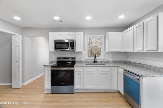 kitchen featuring light stone countertops, white cabinetry, sink, light hardwood / wood-style flooring, and appliances with stainless steel finishes