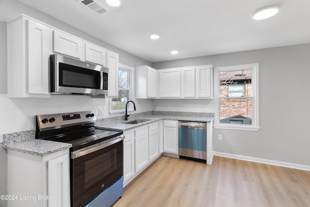 kitchen with white cabinets, sink, light wood-type flooring, light stone counters, and stainless steel appliances