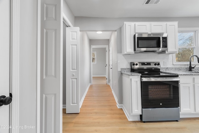 kitchen with decorative backsplash, light stone counters, stainless steel appliances, light hardwood / wood-style floors, and white cabinetry