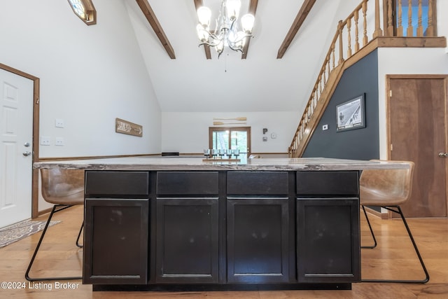 interior space with beam ceiling, pendant lighting, a center island with sink, light hardwood / wood-style flooring, and a chandelier