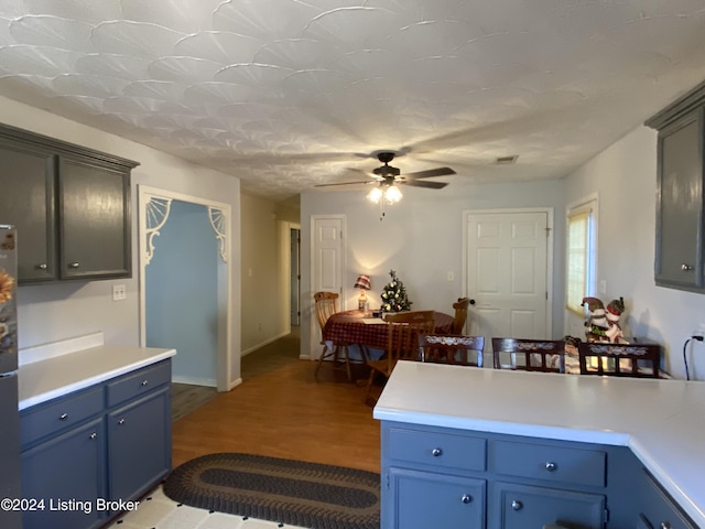 kitchen featuring wood-type flooring, blue cabinets, stainless steel fridge, and ceiling fan