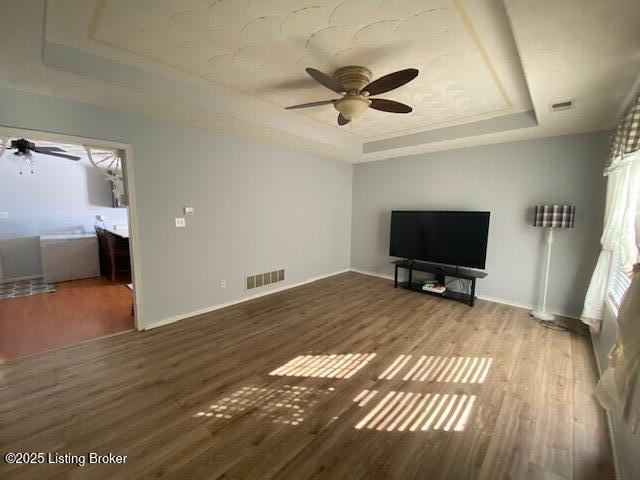 unfurnished living room featuring ceiling fan, hardwood / wood-style flooring, and a tray ceiling