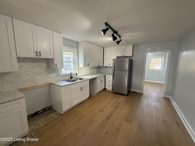 kitchen with sink, stainless steel fridge, a healthy amount of sunlight, white cabinets, and decorative backsplash