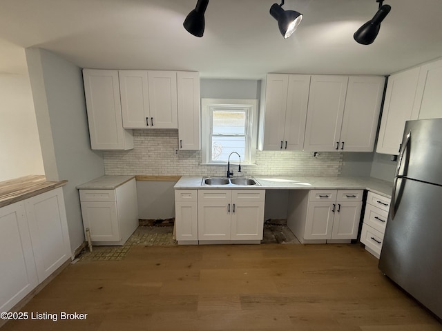 kitchen featuring sink, stainless steel fridge, light hardwood / wood-style flooring, white cabinetry, and decorative backsplash