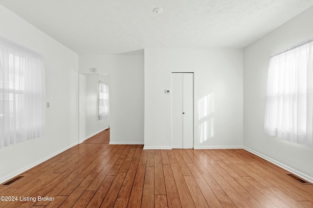 unfurnished room with a textured ceiling and light wood-type flooring