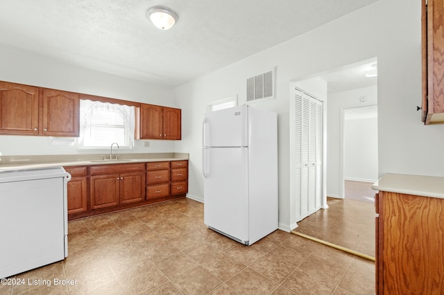 kitchen with a textured ceiling, white appliances, and sink