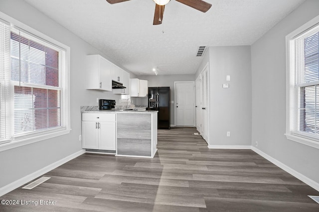 kitchen with a wealth of natural light, white cabinetry, black fridge, and hardwood / wood-style flooring