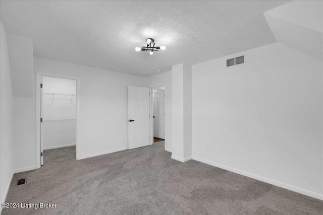 unfurnished bedroom with a walk in closet, a textured ceiling, carpet floors, a closet, and lofted ceiling