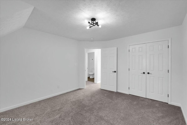 unfurnished bedroom featuring lofted ceiling, carpet floors, a textured ceiling, and a closet