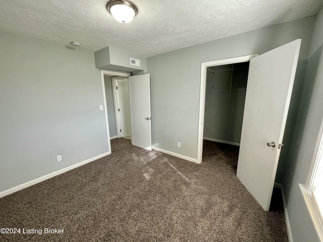 unfurnished bedroom featuring dark carpet, a textured ceiling, a spacious closet, and a closet