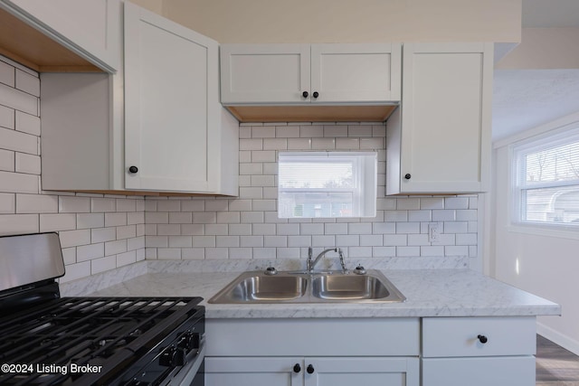 kitchen with white cabinetry, sink, black gas range oven, decorative backsplash, and hardwood / wood-style flooring