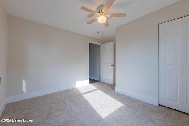 unfurnished bedroom with a closet, light colored carpet, and ceiling fan