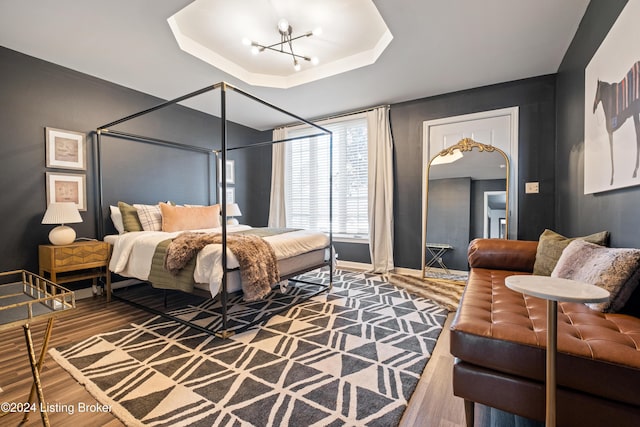 bedroom featuring hardwood / wood-style flooring, a raised ceiling, and an inviting chandelier