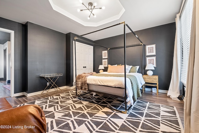 bedroom with hardwood / wood-style floors, a notable chandelier, a tray ceiling, and a closet