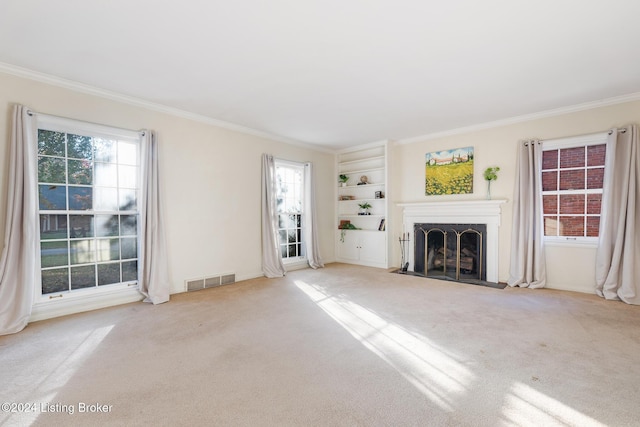 unfurnished living room featuring built in shelves, light colored carpet, and ornamental molding