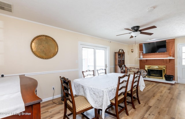 dining space with a textured ceiling, ceiling fan, crown molding, light hardwood / wood-style flooring, and a fireplace