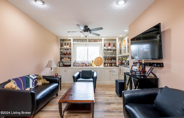 living room featuring ceiling fan, a textured ceiling, and light wood-type flooring