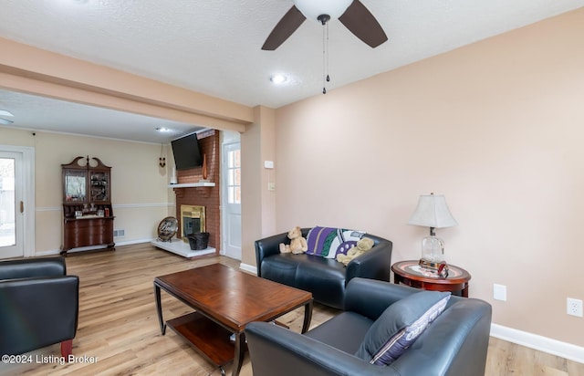 living room featuring ceiling fan, a fireplace, a textured ceiling, and light wood-type flooring