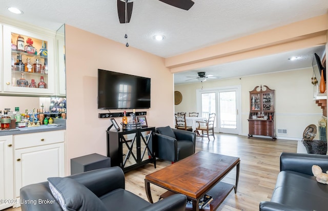 living room featuring ceiling fan, light wood-type flooring, a textured ceiling, and bar area