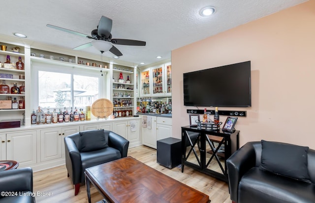 living room with bar, ceiling fan, light hardwood / wood-style flooring, and a textured ceiling