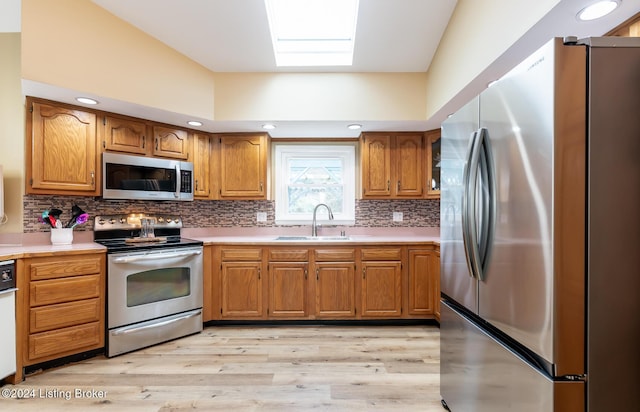 kitchen featuring backsplash, a skylight, stainless steel appliances, sink, and light hardwood / wood-style floors