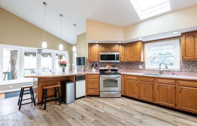 kitchen featuring pendant lighting, high vaulted ceiling, sink, appliances with stainless steel finishes, and light hardwood / wood-style floors