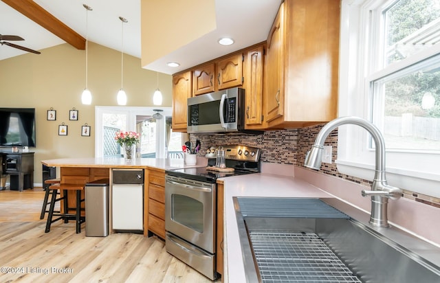 kitchen with pendant lighting, lofted ceiling with beams, sink, light wood-type flooring, and appliances with stainless steel finishes