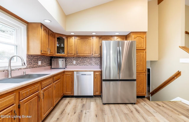 kitchen with sink, stainless steel appliances, backsplash, vaulted ceiling, and light wood-type flooring