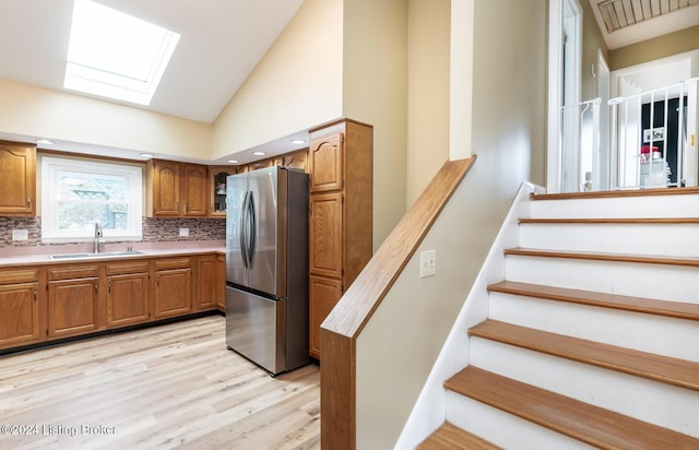 kitchen featuring backsplash, a skylight, stainless steel fridge, and sink