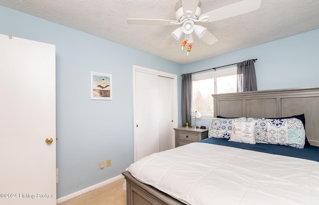 bedroom with ceiling fan, a closet, light colored carpet, and a textured ceiling