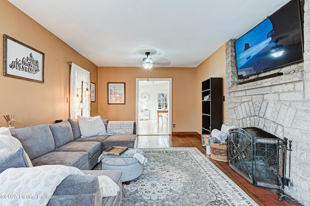 living room featuring ceiling fan, a stone fireplace, and hardwood / wood-style floors