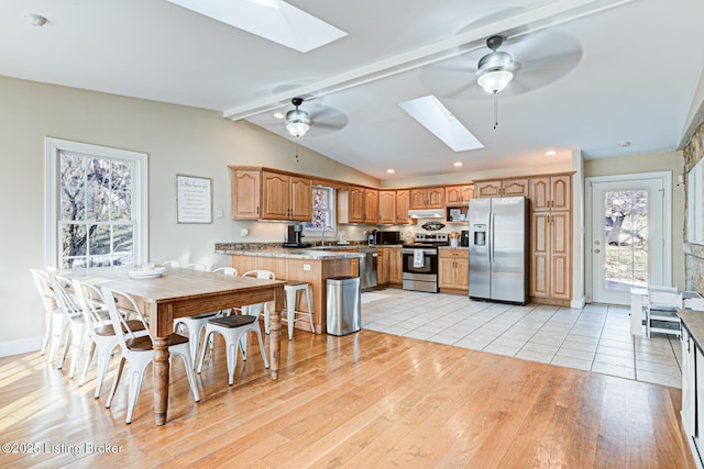 kitchen with a kitchen breakfast bar, ceiling fan, kitchen peninsula, stainless steel appliances, and light hardwood / wood-style flooring