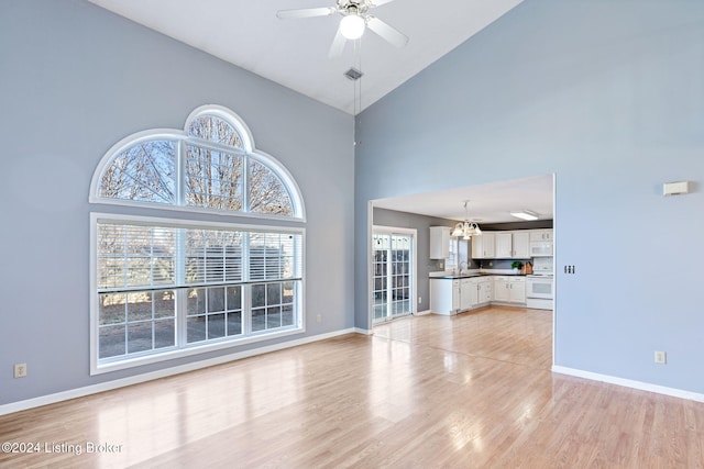 unfurnished living room with high vaulted ceiling, ceiling fan with notable chandelier, and light wood-type flooring