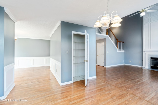 interior space with a high end fireplace, light wood-type flooring, ceiling fan with notable chandelier, and crown molding