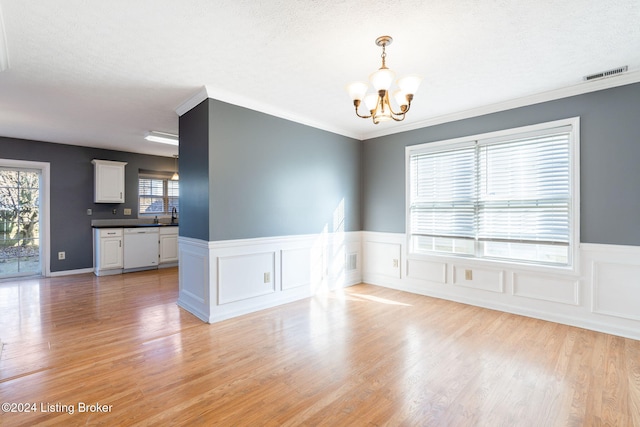 empty room featuring a notable chandelier, ornamental molding, a textured ceiling, and light hardwood / wood-style flooring