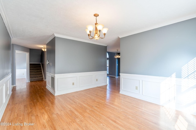 spare room featuring light hardwood / wood-style floors, a chandelier, a textured ceiling, and ornamental molding