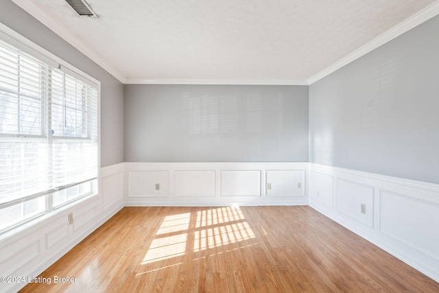 empty room with a wealth of natural light, crown molding, and light wood-type flooring