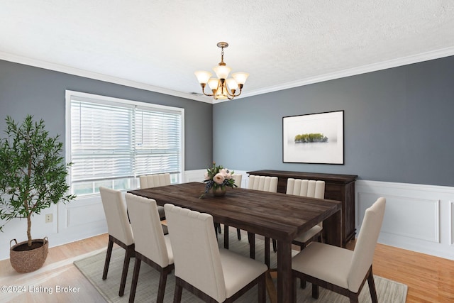 dining space featuring a notable chandelier, light hardwood / wood-style floors, ornamental molding, and a textured ceiling