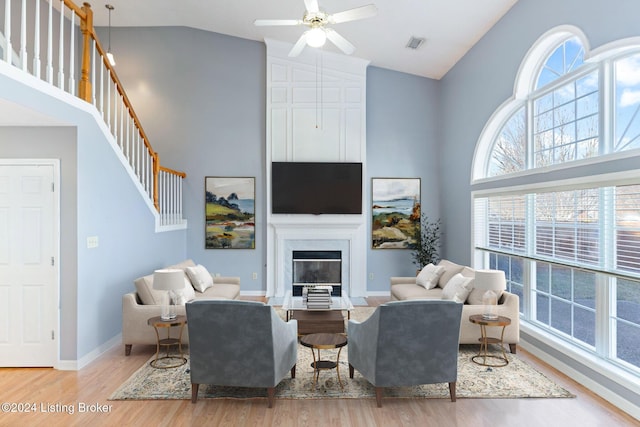 living room featuring ceiling fan, a large fireplace, high vaulted ceiling, and light hardwood / wood-style flooring