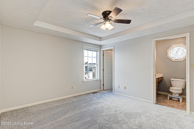 unfurnished bedroom with connected bathroom, a raised ceiling, light colored carpet, ceiling fan, and a textured ceiling