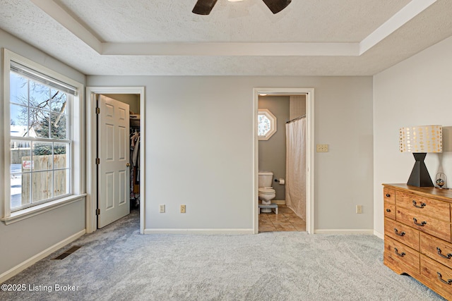 unfurnished bedroom featuring a spacious closet, ensuite bathroom, a raised ceiling, a closet, and ceiling fan