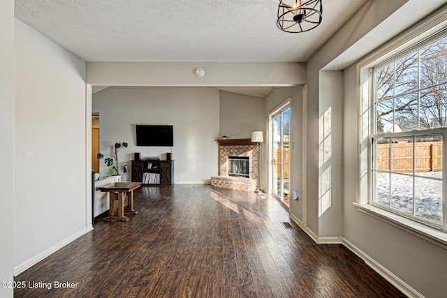 interior space with a healthy amount of sunlight, a brick fireplace, an inviting chandelier, and dark hardwood / wood-style floors