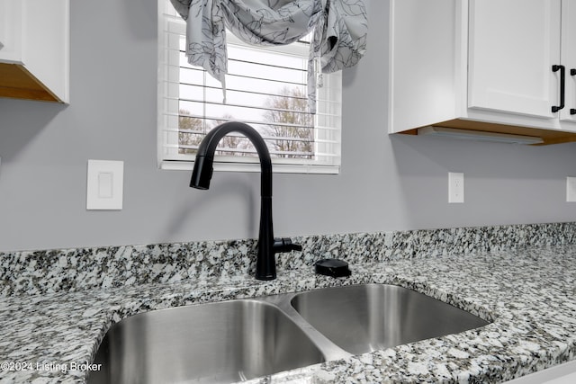 interior details with white cabinets, light stone countertops, and sink