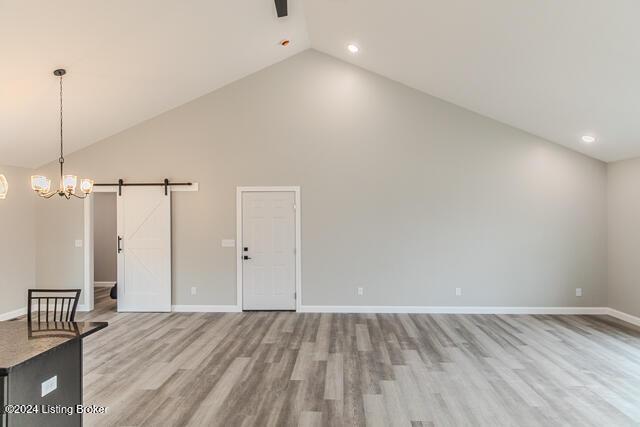 unfurnished living room featuring a barn door, light wood-type flooring, high vaulted ceiling, and a chandelier