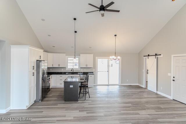 kitchen featuring a breakfast bar, a kitchen island, a barn door, white cabinetry, and stainless steel refrigerator