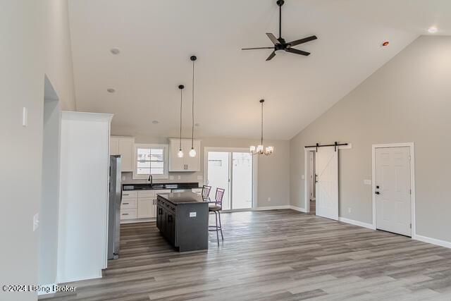 kitchen with a barn door, decorative light fixtures, high vaulted ceiling, white cabinets, and a center island